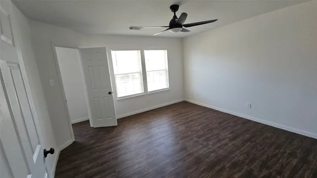 an empty room with wooden floor fan and windows
