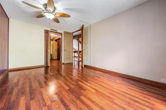 a view of an empty room with wooden floor and a ceiling fan