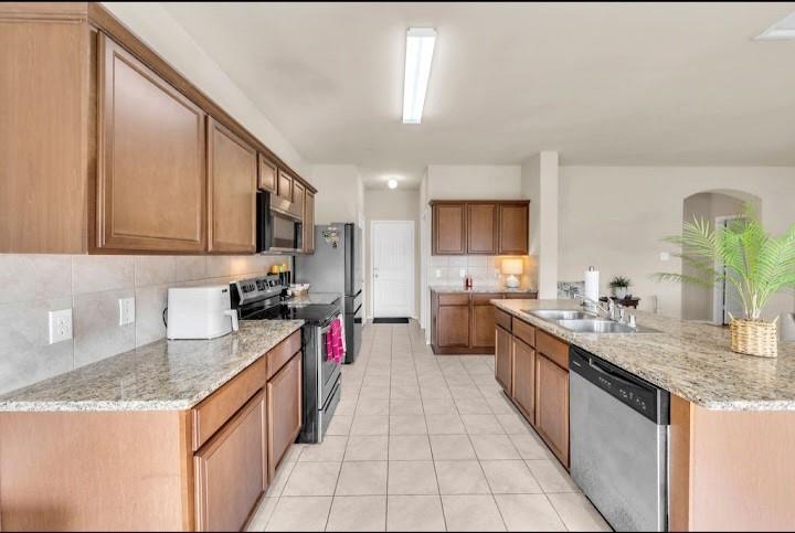 2315 Julia Lane Forney, TX 75126 - Photo 26 of 35 Kitchen with stainless steel appliances, light stone countertops, brown cabinets, light tile patterned floors, and tasteful backsplash