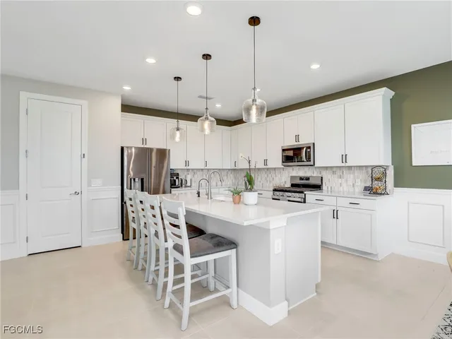 a kitchen with stainless steel appliances kitchen island a table chairs microwave and white cabinets