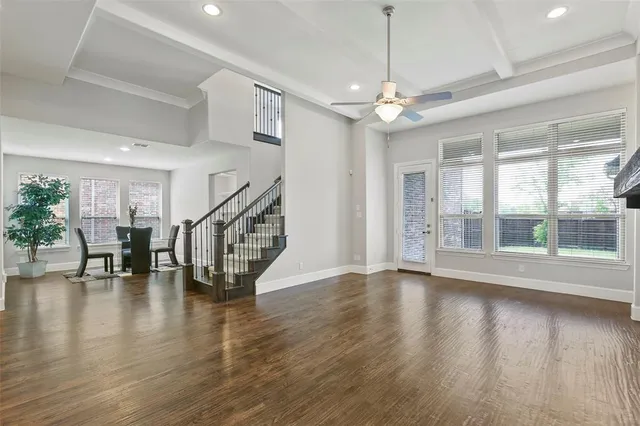 a view of an empty room with wooden floor a ceiling fan and windows