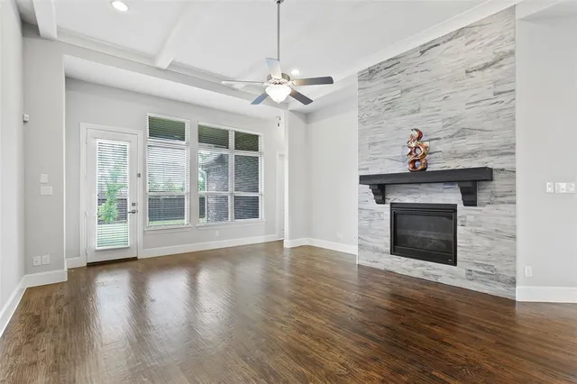 a living room with wooden floor a fireplace a ceiling fan and windows