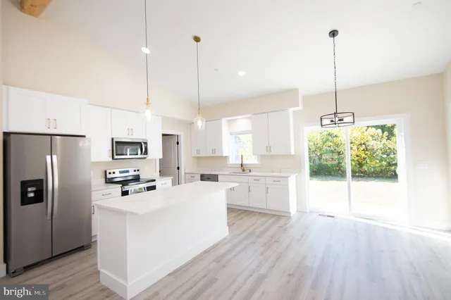 a kitchen with stainless steel appliances kitchen island granite countertop a stove a refrigerator a sink a center island and wooden floor