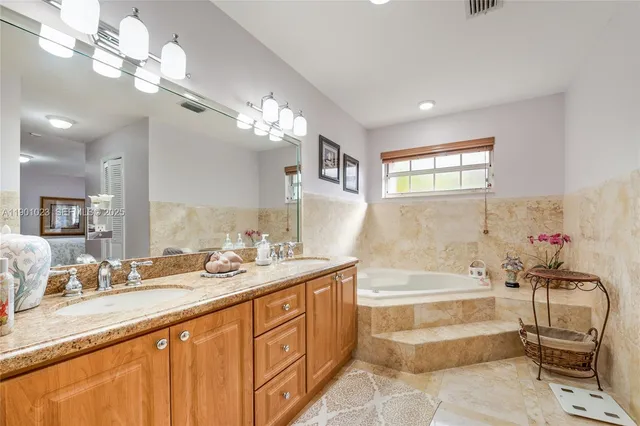 a spacious bathroom with a granite countertop double vanity sink a mirror and a bathtub