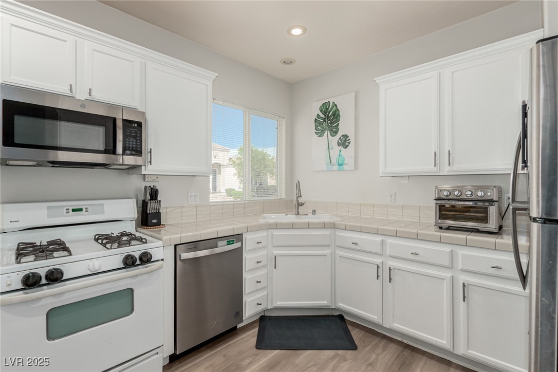 6125 Powdermill Street Las Vegas, NV 89148 - Photo 8 of 33 Kitchen with stainless steel appliances, tile countertops, white cabinets, recessed lighting, and light wood-style flooring