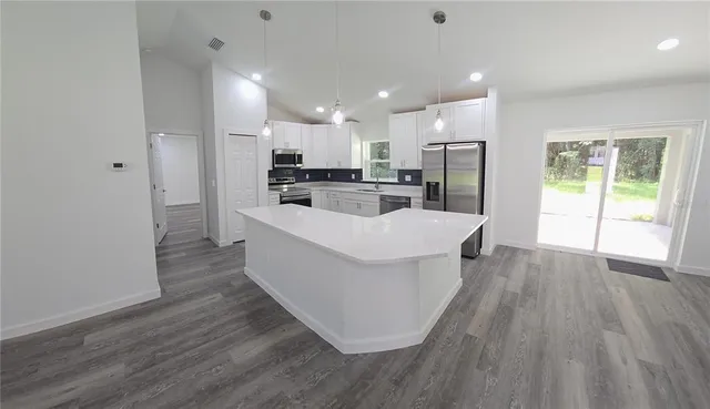 a large white kitchen with wooden floor and stainless steel appliances