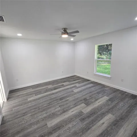 an empty room with wooden floor ceiling fan and windows