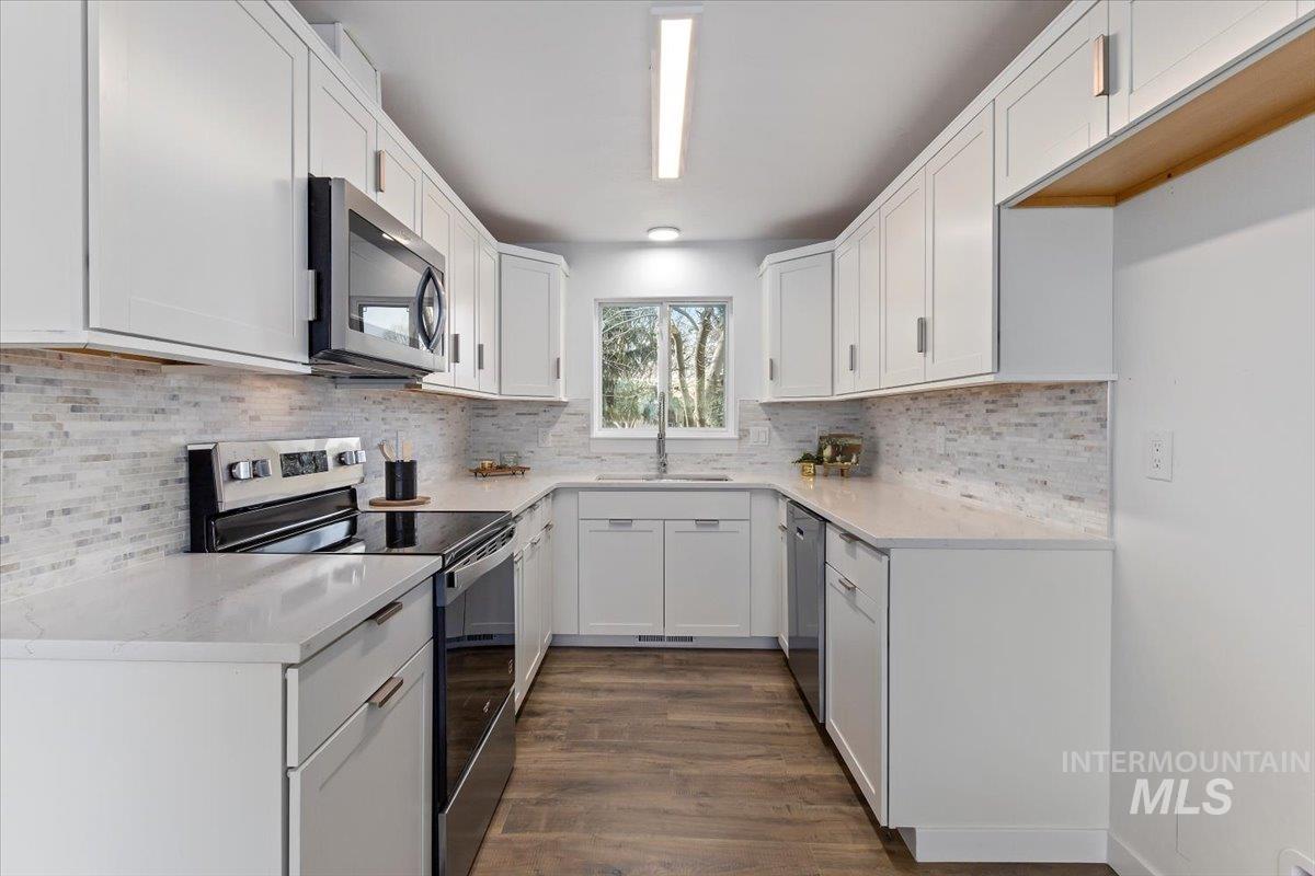 1184 Starfire Street Twin Falls, ID 83301 - Photo 12 of 34 Kitchen with appliances with stainless steel finishes, white cabinetry, dark wood-style flooring, and light stone countertops