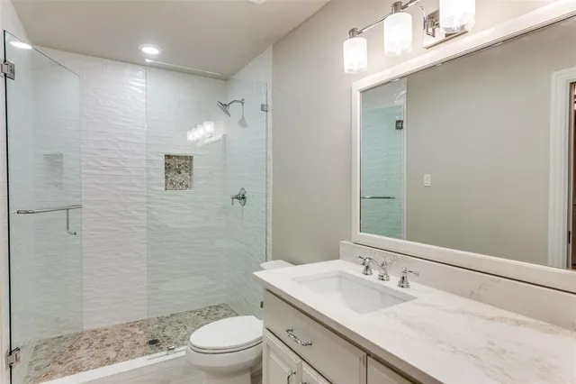 a bathroom with a granite countertop sink a toilet a mirror and shower