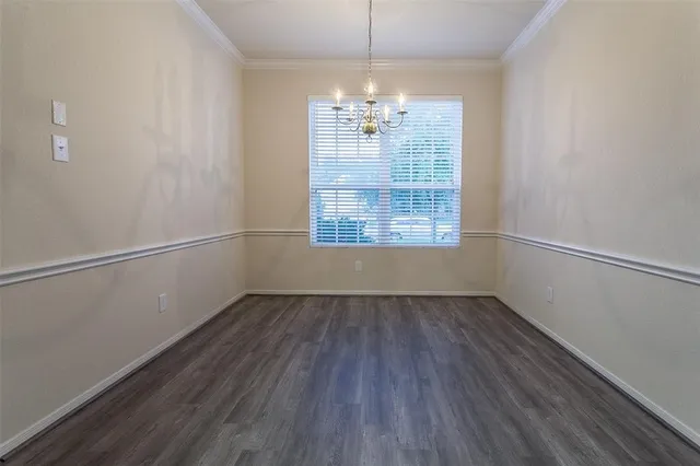 an empty room with wooden floor chandelier and windows