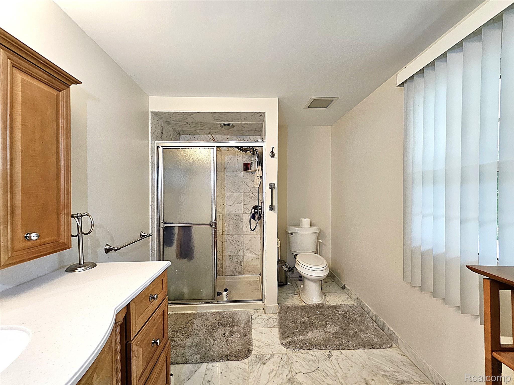 1114 Chaffer Drive Rochester, MI 48306 - Photo 43 of 50 Bathroom featuring a vanity with wood cabinetry and a white countertop, a shower with a sliding glass door and tile surround, and marble-finish flooring