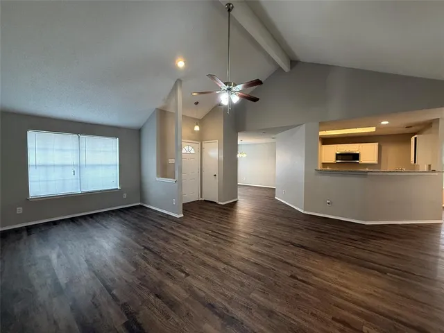 an empty room with wooden floor a ceiling fan a kitchen view and a fireplace