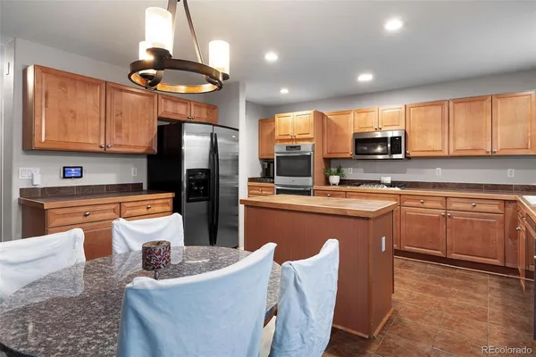 a kitchen with stainless steel appliances granite countertop a refrigerator a stove a sink a dining table and chairs with wooden floor