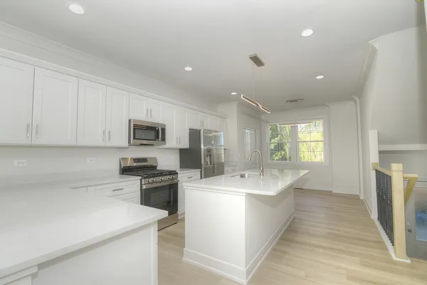 a kitchen with stainless steel appliances a sink dishwasher a stove top oven a refrigerator with white cabinets and wooden floor