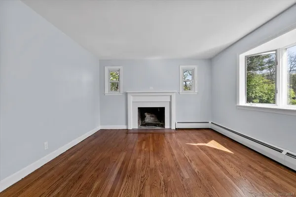 a view of an empty room with wooden floor a fireplace and a window