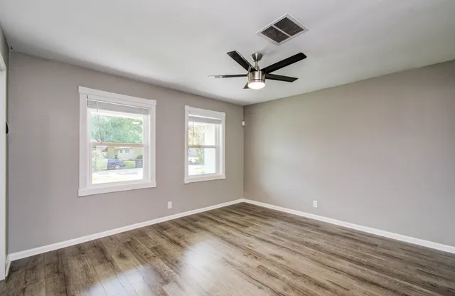 a view of empty room with wooden floor and fan