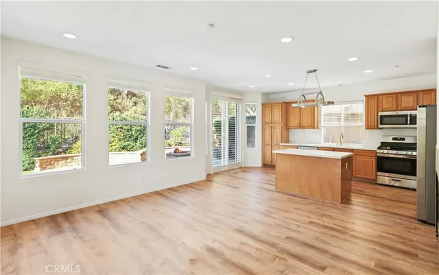 a large kitchen with stainless steel appliances granite countertop a stove top oven a sink dishwasher a refrigerator and white cabinets with wooden floor