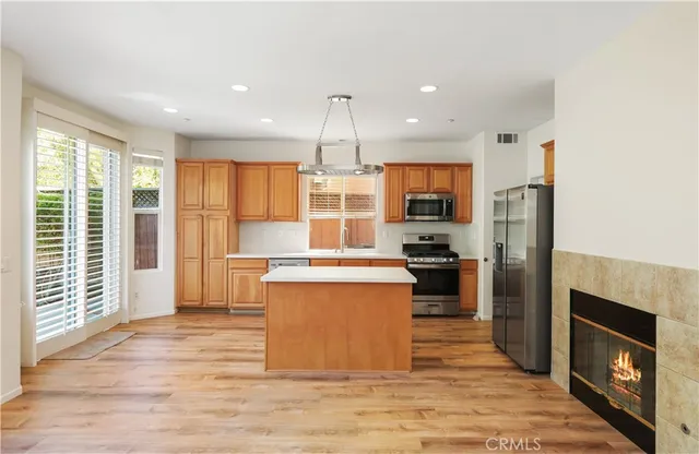 a kitchen with stainless steel appliances granite countertop a stove top oven a sink dishwasher a refrigerator and a fireplace with wooden floor
