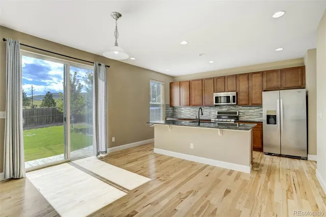 a room with stainless steel appliances granite countertop a refrigerator a sink dishwasher a stove and a large window with wooden floor