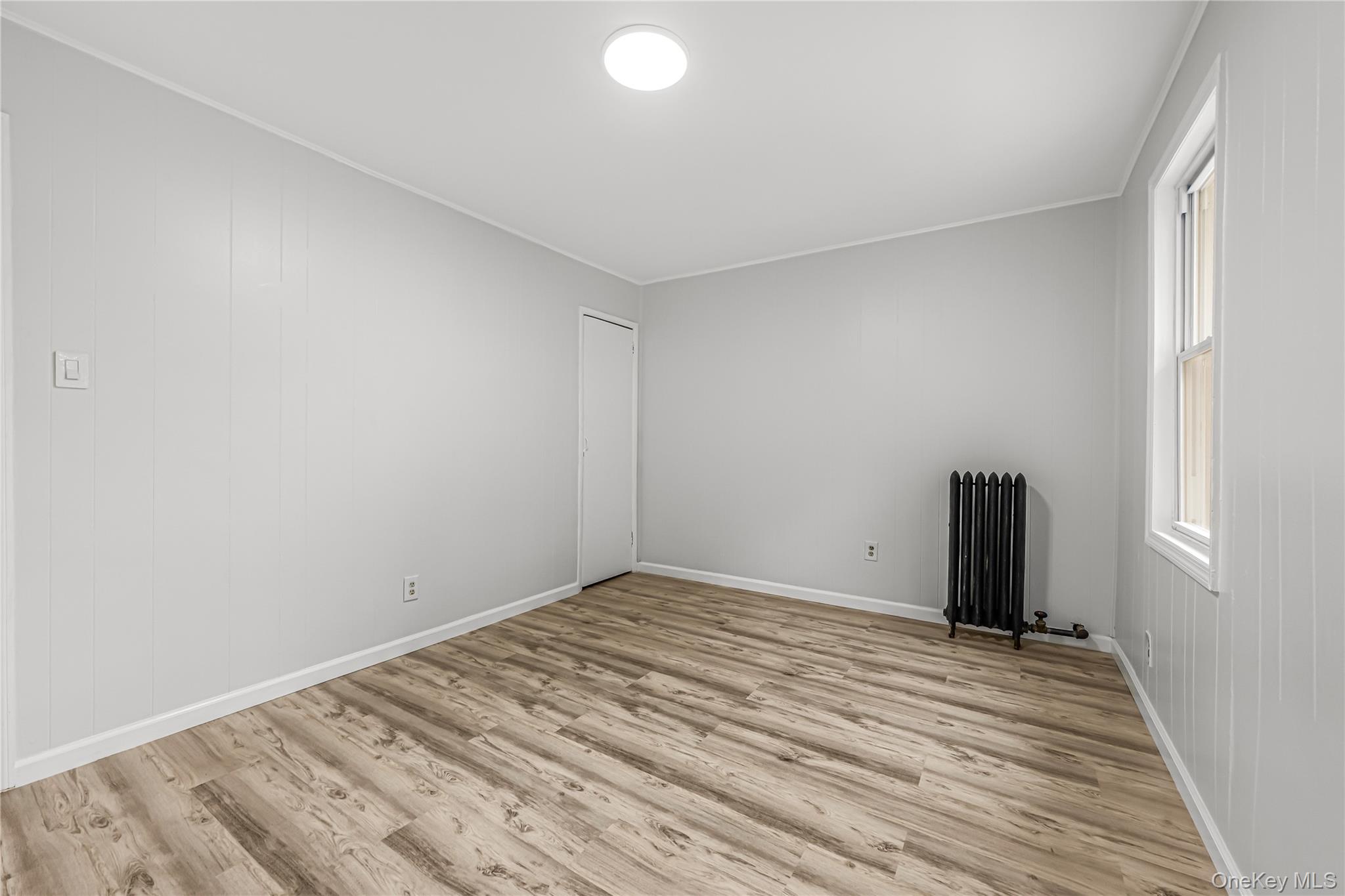 173-43 103rd Road Queens, NY 11433 - Photo 16 of 43 Wood-finish flooring, white paneling, ceiling-mounted light fixture, white trim, and a window with white casing