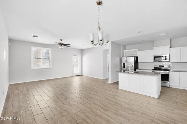 an empty room with wooden floor chandelier and windows