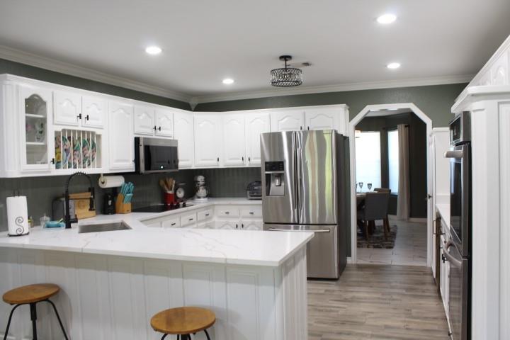 2020 Arbor Bend Road Bonham, TX 75418 - Photo 8 of 19 Modern kitchen featuring white shaker-style cabinetry with glass-front upper doors, stainless steel appliances, white quartz countertops with waterfall island edge, recessed lighting throughout, and wood-finish flooring that extends into the adjoining dining area