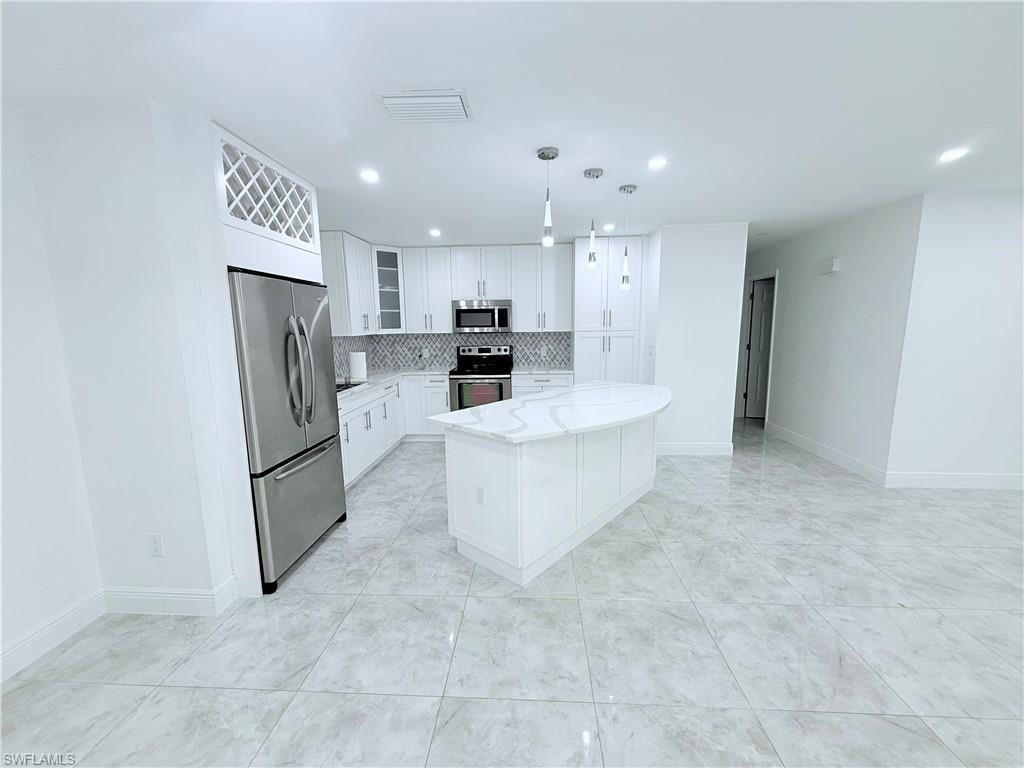 3330 13th Avenue Southwest Naples, FL 34117 - Photo 31 of 50 a large kitchen with a refrigerator a stove a sink dishwasher and white cabinets with wooden floor