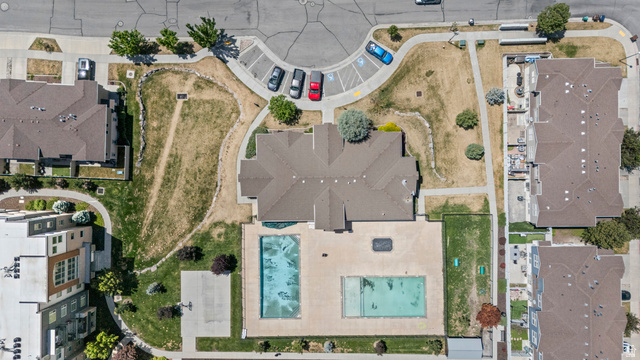 8248 South Resaca Drive, Unit J10 Sandy, UT 84070 - Photo 27 of 40 Community amenities featuring two swimming pools, a central building with a brown shingle roof, a designated parking area, and landscaped green spaces with established trees