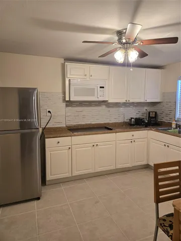a kitchen with granite countertop a refrigerator a sink and white cabinets