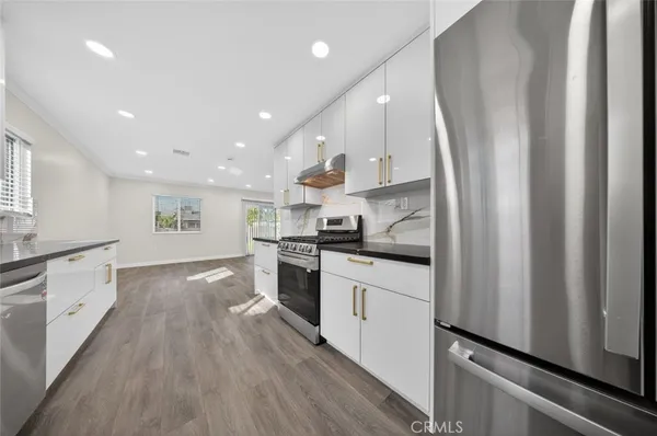 a kitchen with stainless steel appliances granite countertop a refrigerator a sink dishwasher a stove and white countertops with wooden floor