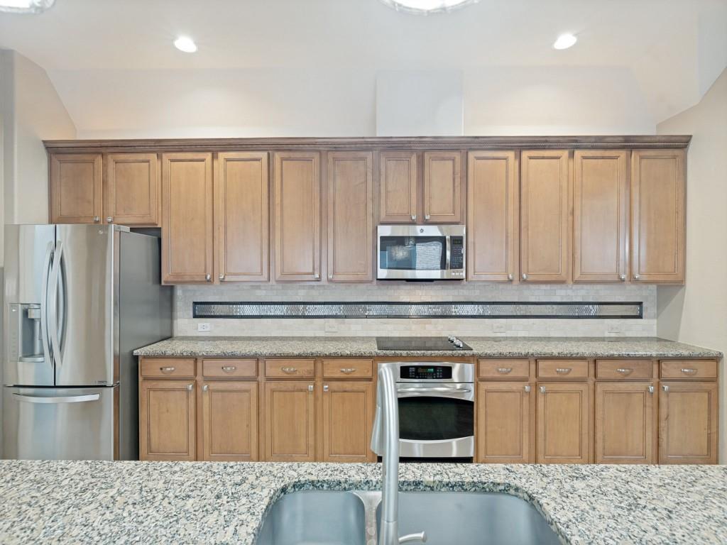 10032 Bell Rock Road Frisco, TX 75035 - Photo 13 of 23 Full kitchen featuring extensive wood cabinetry, stainless steel appliances, granite countertops, and a tile backsplash.
