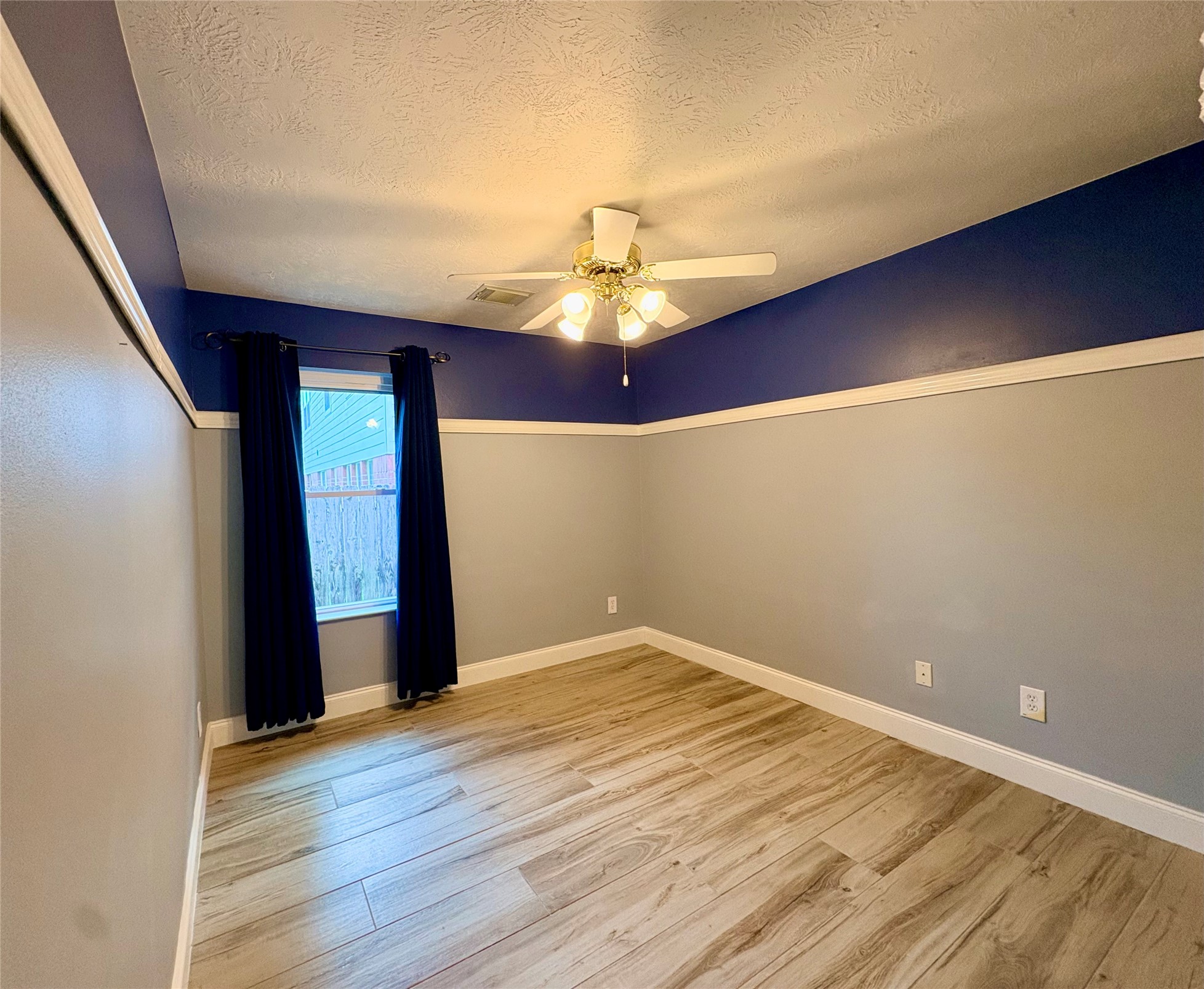 15410 Redbud Berry Way Cypress, TX 77433 - Photo 32 of 49 This room features wood-style flooring, a ceiling fan, and a bold blue and gray color scheme. A window with dark curtains allows natural light, and the space has a clean, modern look.
