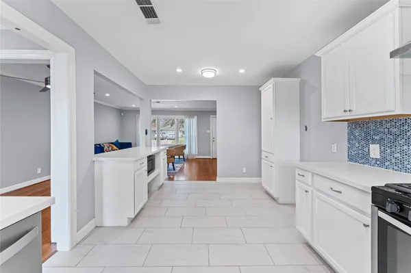 a large white kitchen with cabinets a sink a window and stainless steel appliances