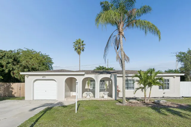 a view of a white house with a yard and palm trees