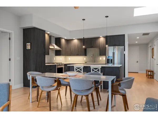a kitchen with stainless steel appliances kitchen island granite countertop a dining table chairs and a refrigerator