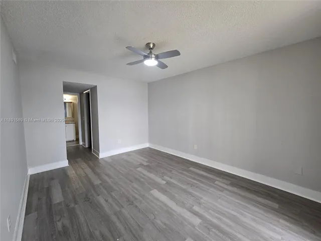 a view of an empty room with wooden floor and a ceiling fan