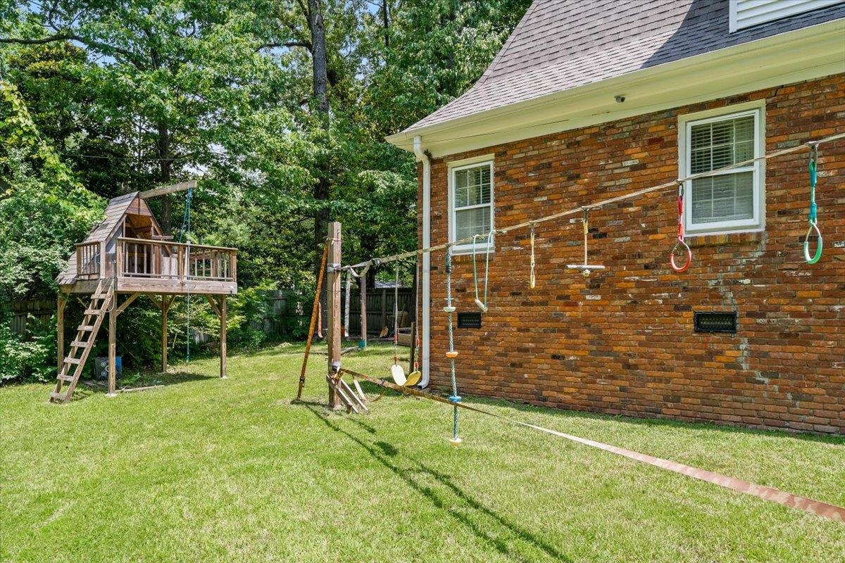 1273 Brookfield Road Memphis, TN 38119 - Photo 36 of 40 Spacious backyard featuring a multi-level wooden play structure, swing set, and a brick exterior with white-framed windows