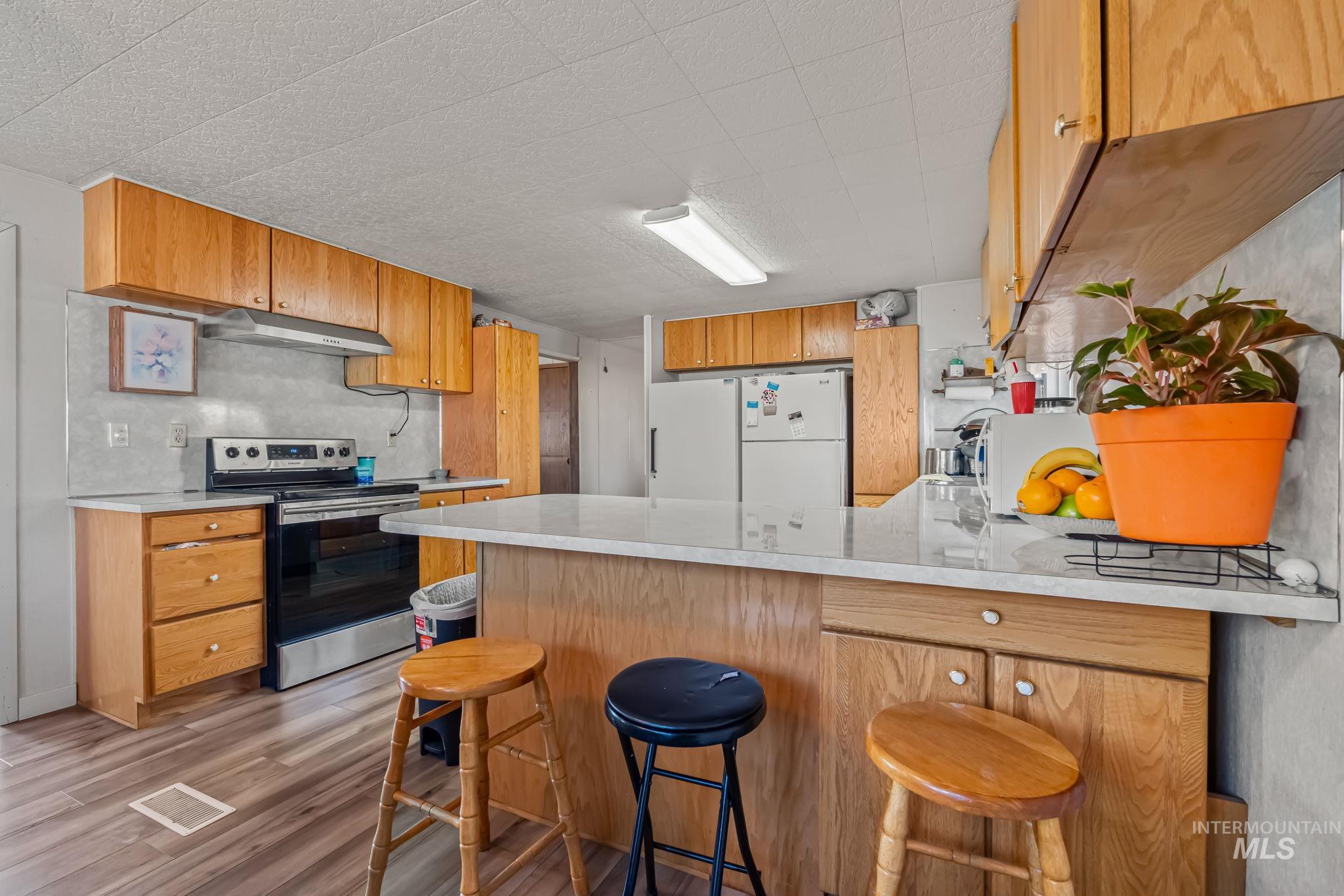 11234 George Street Nampa, ID 83651 - Photo 13 of 25 Kitchen with a peninsula, white appliances, a kitchen breakfast bar, light countertops, and light wood-style flooring