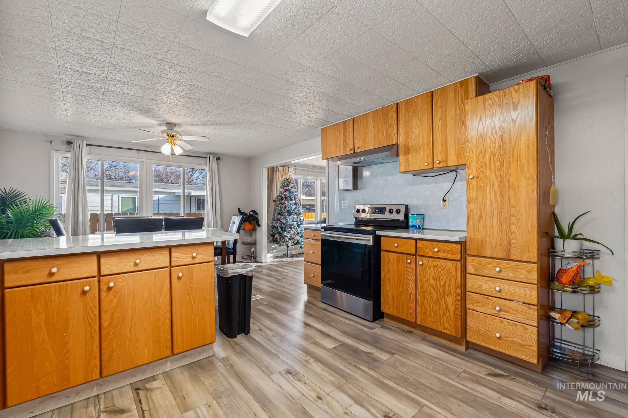 11234 George Street Nampa, ID 83651 - Photo 15 of 25 Kitchen featuring stainless steel electric stove, brown cabinets, light wood finished floors, a ceiling fan, and under cabinet range hood