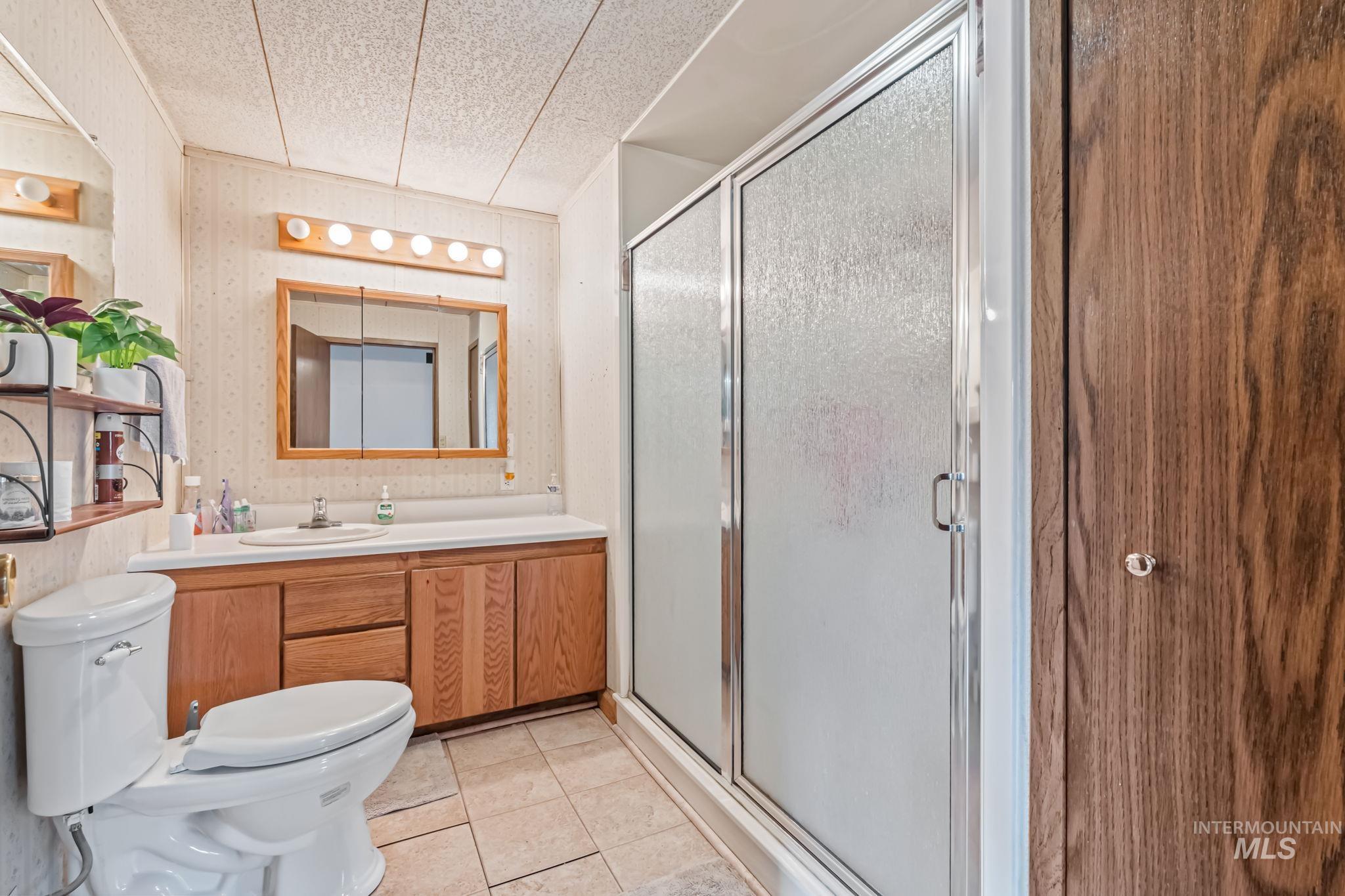11234 George Street Nampa, ID 83651 - Photo 22 of 25 Bathroom featuring a stall shower, light tile patterned flooring, vanity, and wallpapered walls