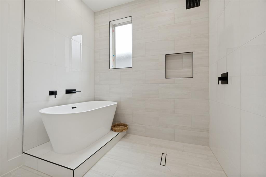 1143 Riverwood Road Dallas, TX 75217 - Photo 22 of 24 Modern bathroom featuring a freestanding soaking tub on a tiled platform, a walk-in shower with a linear drain, and matte black fixtures