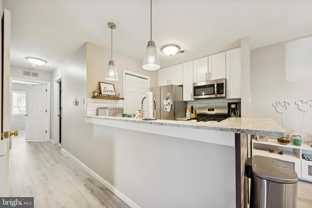 a kitchen with stainless steel appliances a stove a sink dishwasher a refrigerator white cabinets and wooden floor