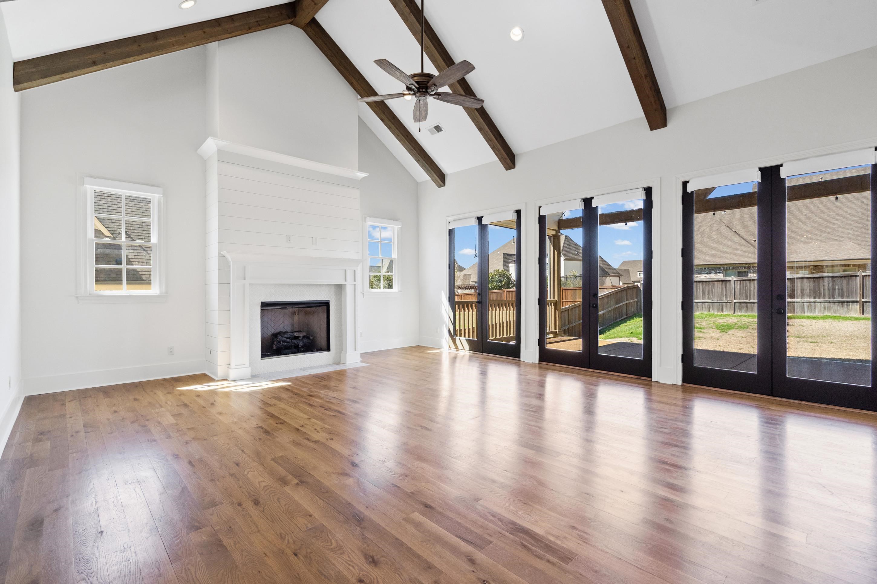 12608 Bravo Road Collierville, TN 38017 - Photo 7 of 40 Unfurnished living room featuring wood-type flooring, a ceiling fan, a fireplace with flush hearth, lofted ceiling, and french doors