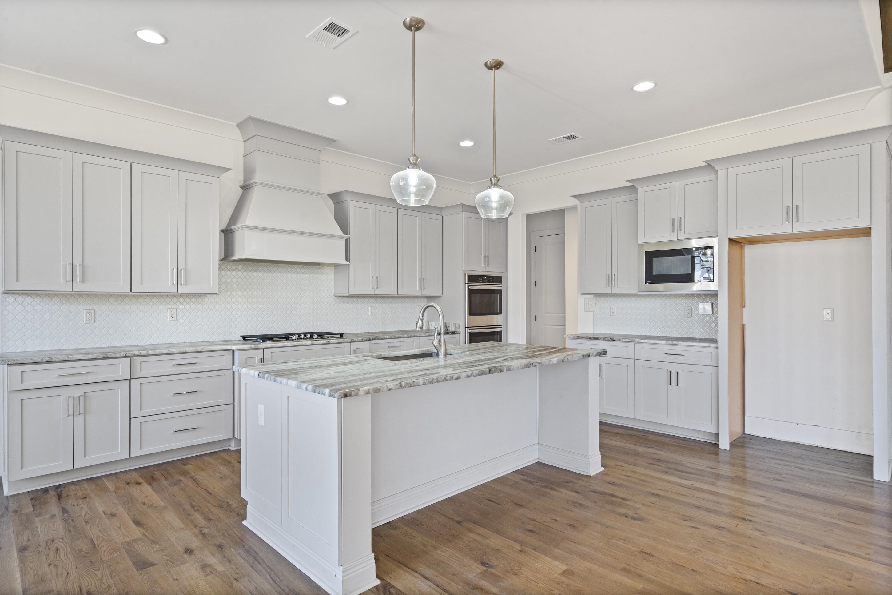 12608 Bravo Road Collierville, TN 38017 - Photo 9 of 40 Kitchen with light stone counters, crown molding, decorative backsplash, a kitchen island with sink, and dark wood-style floors