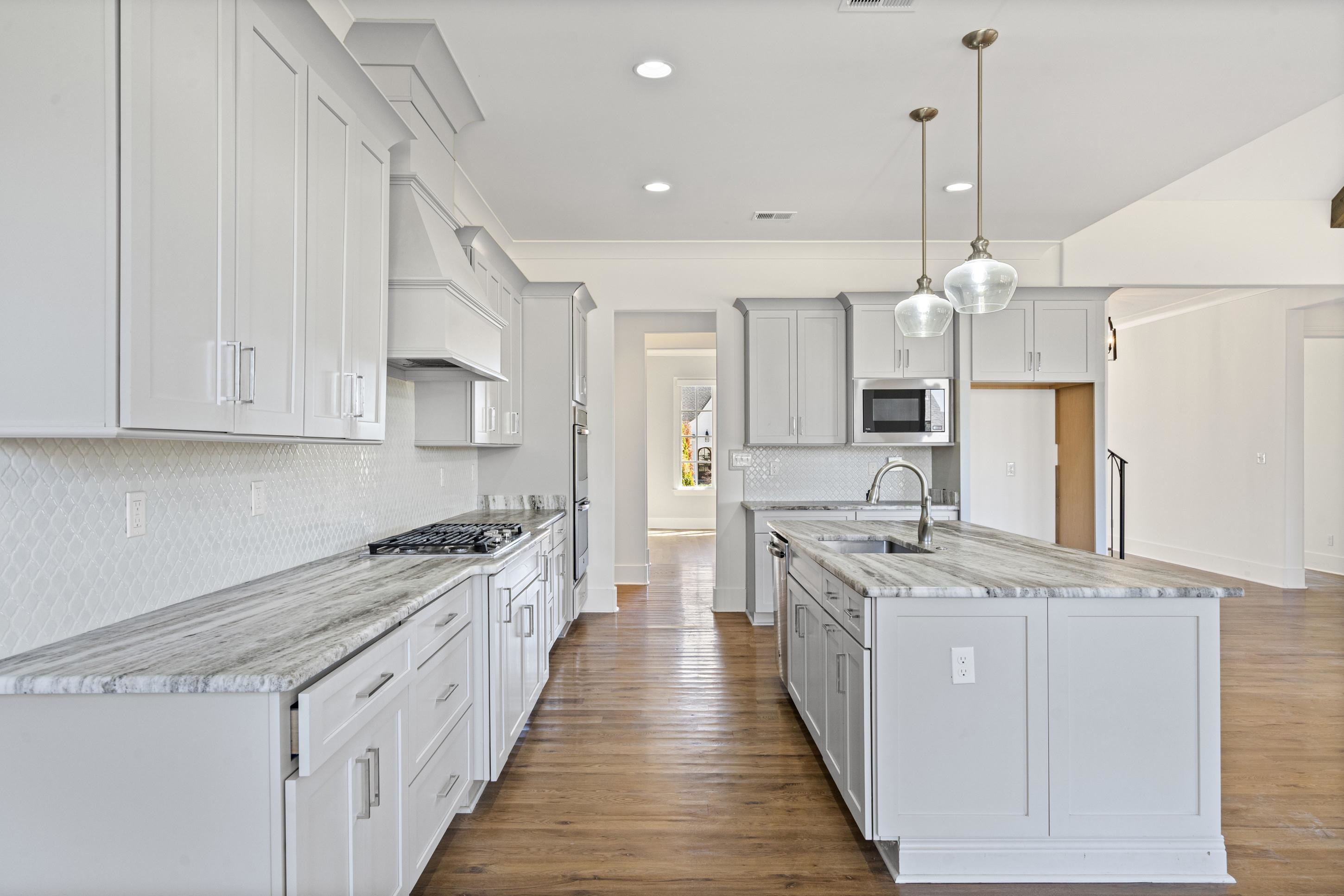 12608 Bravo Road Collierville, TN 38017 - Photo 10 of 40 Kitchen featuring dark wood-type flooring, a kitchen island with sink, pendant lighting, light stone counters, and tasteful backsplash