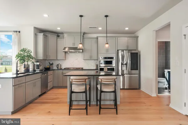 a kitchen with stainless steel appliances granite countertop a refrigerator a stove a sink a dining table and chairs with wooden floor