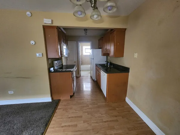 a view of a hallway with wooden floor and a kitchen space