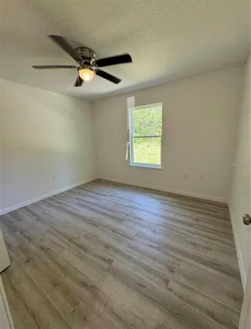 an empty room with wooden floor ceiling fan and windows