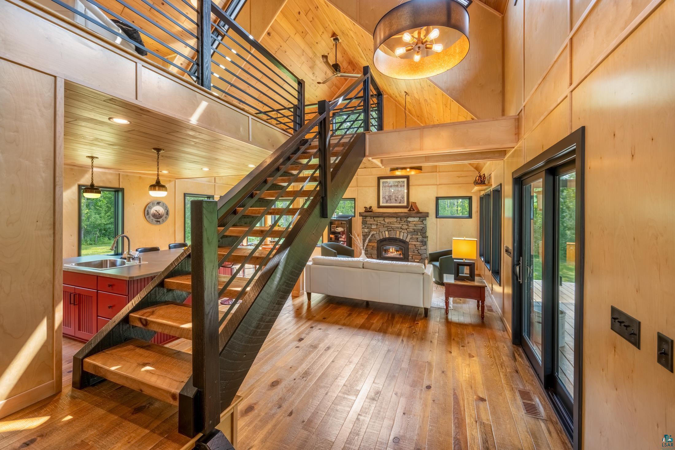 3778 East County Road Barnum, MN 55707 - Photo 19 of 52 Vaulted ceiling with wood-finish paneling, exposed wood beams, open-tread staircase with metal railings, stone fireplace, and wood-finish flooring