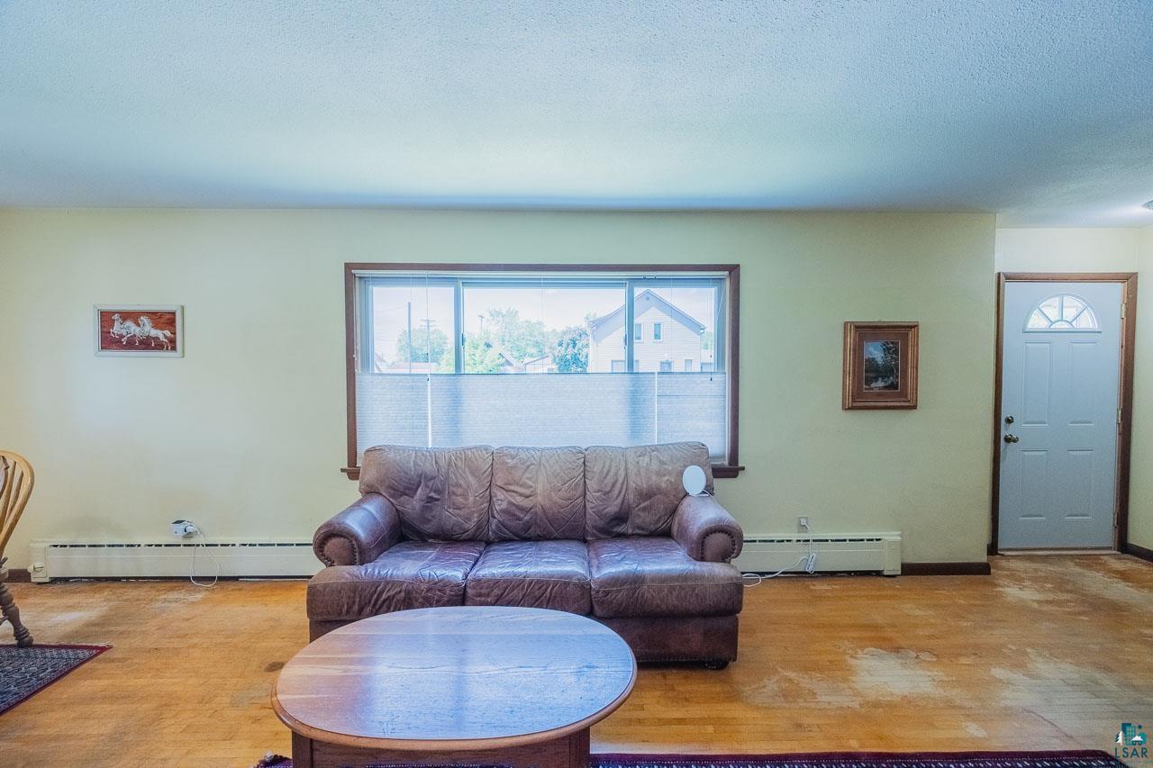 101 2nd Avenue North Biwabik, MN 55708 - Photo 5 of 44 Living area featuring wood-finish flooring, a large window with horizontal blinds, and a white entry door with a decorative glass insert